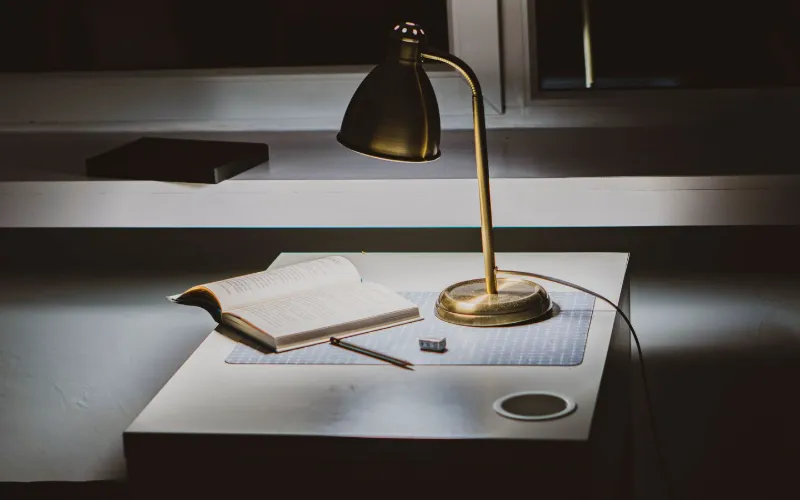 A desk with a brass lamp, an open book and a pen